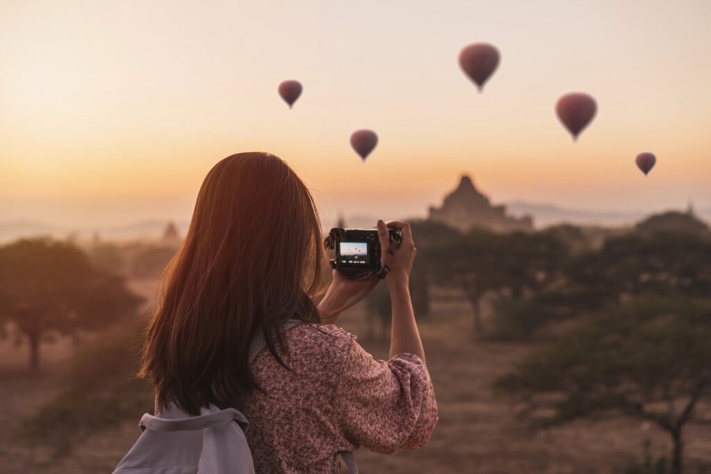 Young woman with camera enjoying the view of hot air balloons over ancient pagoda at Bagan