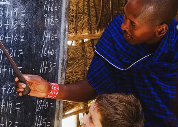 A person putting on Maasai tribe cloth, teaching a young white child, arithmentics and numbers