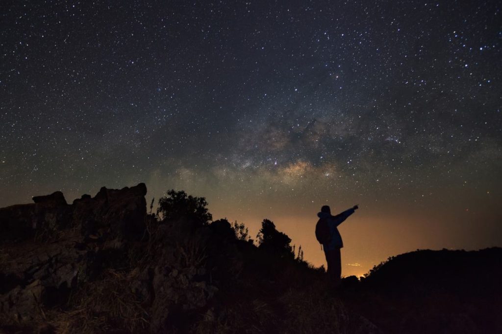 A Man is standing next to the milky way galaxy pointing on a bright star