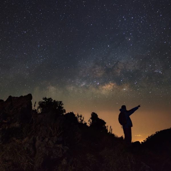 A Man is standing next to the milky way galaxy pointing on a bright star